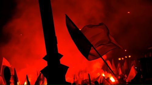 Protesters hold flags aloft in a smoke-filled red scene, evoking themes of nationalism and collective unrest.