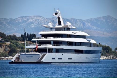 A sleek, multi-deck luxury yacht anchored off a quiet coastline, symbolizing extreme wealth and exclusivity amid natural beauty.